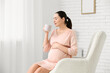 © Pixel-Shot - Beautiful young pregnant woman with cup of tea sitting in armchair in living room