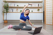 © Natee Meepian - Wellness Routine. Young woman stretching during home workout with laptop.