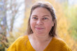 © kittyfly - Mature woman with thoughtful neutral expression outdoors in autumn park, Mature female face with neutral emotion, facial wrinkles around eyes, soft natural light, calm mood, seasonal portrait concept