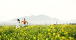 © peopleimages.com - Canola field, running and couple in nature for adventure, fun and exploring together on summer holiday. Space, outdoor and man with woman for bonding in flower environment in countryside for vacation