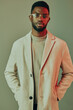 © SHOTPRIME STUDIO - Stylish young man in a light beige coat and glasses against a muted green background, embodying modern fashion and confidence
