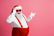 © deagreez - Santa Claus in red suspenders and white coat smiles and points on a pink background for a playful festive Christmas mood