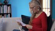 © Robert Peak - Frustrated middle-aged woman with glasses sitting on a sofa appears stressed, angry, while reading a letter. She rests her hand on her forehead, showing signs of concern.