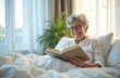 © miss irine - Happy smiling senior woman reads book in bed. Elderly female with glasses enjoys literature resting in bright bedroom. Mature lady relaxes with novel in cozy comfortable home.