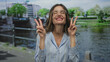 © Krakenimages.com - Young woman with glasses holds up hands in victory sign over canal water on street; joy celebration.