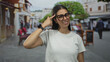 © Krakenimages.com - Woman points finger to temple at outdoor restaurant terrace on street wearing glasses and white tshirt, smiling slightly; thinking playful.