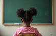 © miss irine - Little african girl sits on chair opposite blackboard. Pupil looking at green school board in classroom. Elementary schoolkid with afro hair in pink tshirt studies in class or lesson.