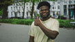 © Krakenimages.com - Man showing thumbs up on street in front of white apartment building and green park hedges, smiling with bare hand and thumb visible; confidence positivity.