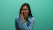 © Krakenimages.com - Woman whispering with a playful expression against a vibrant green background, wearing glasses and a blue shirt, creating an engaging and approachable visual for communication themes
