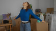 © Krakenimages.com - Woman in blue sweater standing inside new home surrounded by moving boxes and plants in the living room as she stretches with a happy expression
