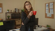 © Krakenimages.com - Woman holding a red cup in a modern office with charts on the wall and a thoughtful expression, showcasing a professional workspace environment.