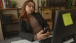 © Krakenimages.com - Businesswoman in glasses with a phone reclines in an office chair at her desk with bookshelves in background showing modern work environment and professional attire.