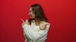 © Krakenimages.com - Woman wearing white sweater pointing sideways against bold red wall background showcases playful young expression and casual style in vibrant isolated setting.