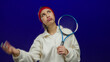 © Krakenimages.com - Woman wiping sweat with hand holds tennis racket against isolated blue background wearing white sweatshirt and red headband depicting tiredness and effort.