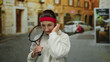 © Krakenimages.com - Woman with racket in city street adjusting headband, showcasing relaxed sporting posture with focus on exercise and urban life.