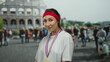 © Krakenimages.com - Woman smiling in front of the iconic roman colosseum wearing a gold medal and red headband, surrounded by a lively outdoor scene, expressing a sense of achievement and joy.