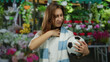 © Krakenimages.com - Woman holding soccer ball in street flower shop, wearing scarf, feeling unwell, surrounded by vibrant city flowers during outdoor scene, expressing discomfort.