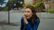 © Krakenimages.com - Woman whispering secret on city street, wearing blue sweater, outdoors, expressing excitement, youthful energy and mystery with a playful gesture.