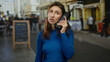 © Krakenimages.com - Young woman holding retro phone on city street, dressed in blue, conveying urban nostalgia amidst a lively outdoor backdrop with blurred pedestrians.