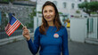 © Krakenimages.com - Woman outdoors in city holding american flag and vote badge on blue sweater, symbolizing civic engagement and pride in the united states.