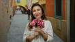 © Krakenimages.com - Woman smiling with pink flowers on a vibrant city street showcasing joyful expression in urban outdoor setting with tattoo visible against charming architectural background.