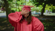 © Krakenimages.com - Graduated young woman in pink cap and gown stands outdoors in a park setting, her hand on her forehead under the sunny trees, reflecting thoughtful and contemplative mood.