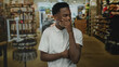 © Krakenimages.com - Young african american man covers mouth with hand while smiling amid shelves in a brightly lit retail store aisle; laughter joy.
