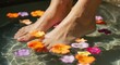 © NN AI - Woman relaxing in spa foot bath with floating flowers. Pedicure and wellness treatment for skin care. Self-care and hydrotherapy concept