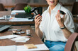 © satura_ - Woman showing makeup brushes and powder jar while sitting at desk. Beauty, confidence, and expression of individuality in modern lifestyle.