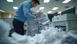 © Pete - Office worker manages huge paper stack. Stands by printer in messy office. Documents piled up, causing big problem. Looks overwhelmed with task. Printing error creates much paper. Common office issue.