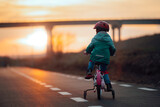 Girl on a Bike with Training Wheels Riding Into the Sunset. Active kid pedaling on her bicycle in the evening  
