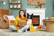© Pixel-Shot - Young woman with plaid and cute Border Collie dog reading book at home on autumn day