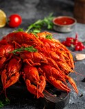 A close-up shot of a pile of vibrant red crustaceans presented on a rustic wooden board, garnished with herbs and a side of sauce