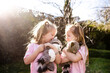 © Austockphoto - Young twin sisters hugging each other while holding raccoon stuffed toy
