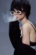 © SHOTPRIME STUDIO - Stylish woman with short black hair wearing sunglasses and blowing smoke in a black outfit and exposed shoulder