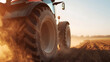 © A2Z AI  - A tractor is driving through a plowed field at sunset, kicking up dust. The focus is on the large tire and the dirt it is kicking up, showing the strength and power of agricultural machines.