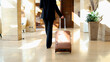 © PeopleVideos - Business executive in a black suit walking through a modern hotel lobby, pulling a brown suitcase for a journey