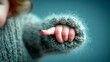 © ardi - A close-up shot focuses on a baby's tiny hand emerging from a warm, fuzzy, knitted sweater sleeve against a soft blue background.
