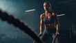 © Andrii - Muscular Young Woman Smiling As She Exercises With Battle Ropes In A Dark Gym, Engaging In Intense Functional Circuit Training