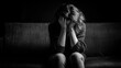 © mila103 - A woman is sitting on a couch in a dark room, holding her head with both hands. She appears to be overwhelmed by her emotions, reflecting a moment of intense sadness or anxiety.
