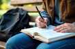 © starush - Woman writing in notebook outdoors on park bench with backpack nearby