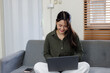 © David - A woman sits comfortably on a soft sofa, focused on her laptop while surrounded by a modern living room with warm lighting and greenery.