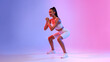 © Prostock-studio - A motivated sportswoman is doing deep squat exercises in white fitwear. The colorful neon pink and blue background enhances her focus during this energizing workout session.