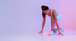 © Prostock-studio - Female athlete is positioned in a crouch start stance on a studio floor illuminated by a vibrant pink neon background. She is focused and prepared to begin her sprint, emphasizing sport motivation.
