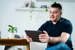 © Austockphoto - A man in his 30s is sitting in a chair, engaging with a tablet in a cosy home setting