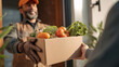 © Jhati - Delivery man in orange cap handing over a box of fresh produce to a person at the door