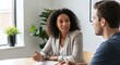 © Lahiru - A confident woman in business attire talks to a man at a desk in a bright office space, surrounded by green plants and natural light creating a calm professional environment
