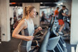 © Dorde - Smiling young woman running on treadmill indoors in modern gym environment with fitness equipment