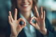 © grey - A cheerful woman makes an OK sign with her fingers, expressing approval and satisfaction in a business context.