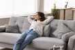 © fizkes - Smiling young female lean back on sofa hands behind head